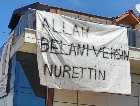  “Nurettin, Allah belanı versin” yazılı pankartı görenler, şaşkınlıklarını gizleyemedi ve bir kez daha baktılar. Seymen Mahallesi’ndeki Hürriyet Caddesi üzerinde bulunan bir binanın cephesine asılan bu pankart, herkesi hayrete düşürdü.