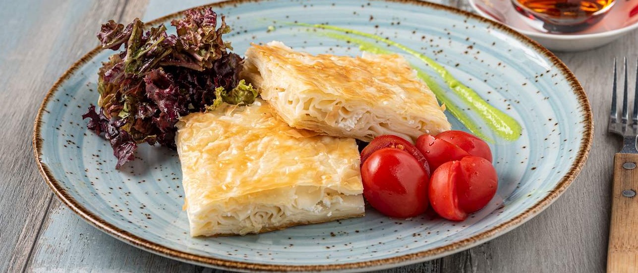 BÖREK: TÜRK MUTFAĞININ LEZZETLİ YANSIMASI

Türk mutfağının vazgeçilmezlerinden biri olan börek, ince yufka tabakalarıyla sarılarak hazırlanan ve çeşitli iç malzemelerle zenginleştirilen bir lezzet şölenidir. Kökeni Osmanlı İmparatorluğu'na dayanan bu enfes yemek, Türkiye'nin her bölgesinde farklı çeşitlerde ve tatlarla sunulmaktadır. Su böreği, kalem böreği, paçanga böreği gibi çeşitler, her biri kendi özgün tadını ve dokusunu sunar. Gül böreği gibi estetik bir sunumla gözleri şenlendiren çeşitler de bulunmaktadır. Türk börekleri, geleneksel lezzetler arasında özel bir yere sahiptir ve Türk kahvaltısının vazgeçilmezlerindendir.
